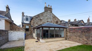 A stone building with a glass conservatory, a paved courtyard, and a grassy area. - St Meddans Mews in Troon (Troon)
