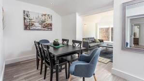 A modern dining area with a black table and chairs, a painting on the wall, and a view into a living room with a sofa and a window. - St Meddans Mews in Troon (Troon)