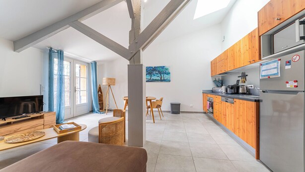 A modern kitchen with wooden cabinets, a stainless steel refrigerator, and a dining area with a table and chairs. - DOMAINE DU FLAMAND - GÎTE LAGUNE (Naujac-sur-Mer)