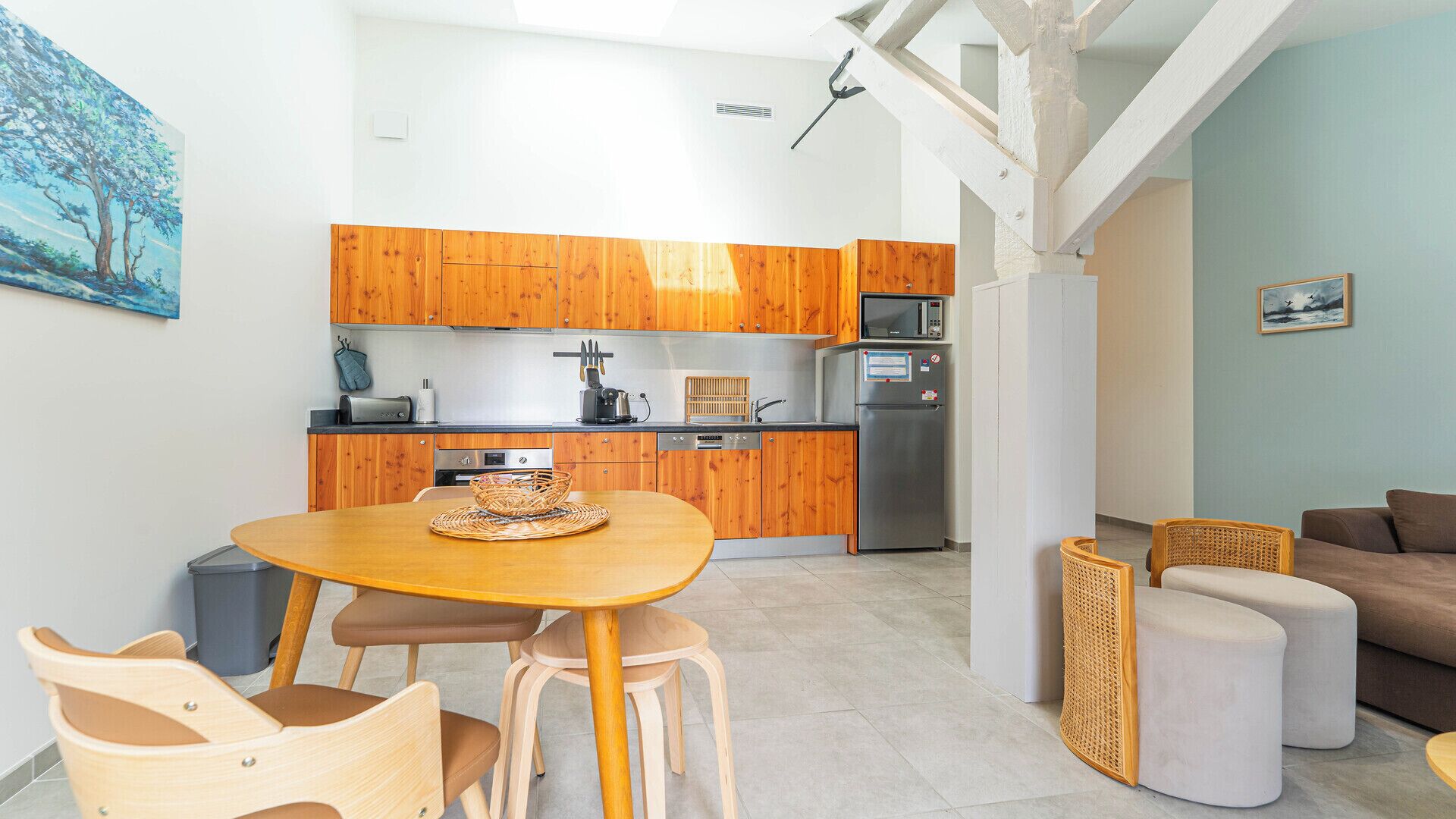 A modern kitchen with wooden cabinets, a dining table with chairs, a refrigerator, and a microwave.
