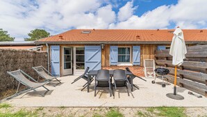 A rustic building with a tiled roof, a wooden fence, and a patio with outdoor furniture. - DOMAINE DU FLAMAND - GÎTE LAGUNE (Naujac-sur-Mer)