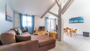 A living room with a brown sofa, a TV, and a dining area with a table and chairs. - DOMAINE DU FLAMAND - GÎTE LAGUNE (Naujac-sur-Mer)