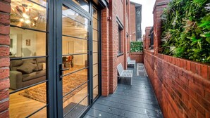 Une ruelle étroite, avec un mur de briques d’un côté et une porte vitrée qui donne sur une pièce contenant un canapé et une table.