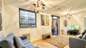 Un salon moderne avec un parquet en chevrons, des canapés gris, une grande fenêtre et un téléviseur.