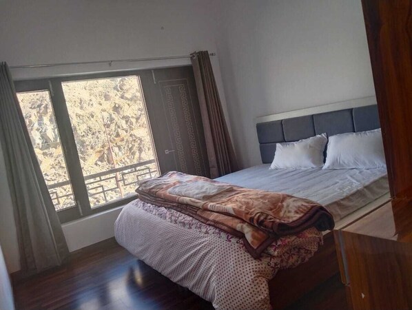 A bedroom with a bed, a window with curtains, and a view of a rocky landscape.
