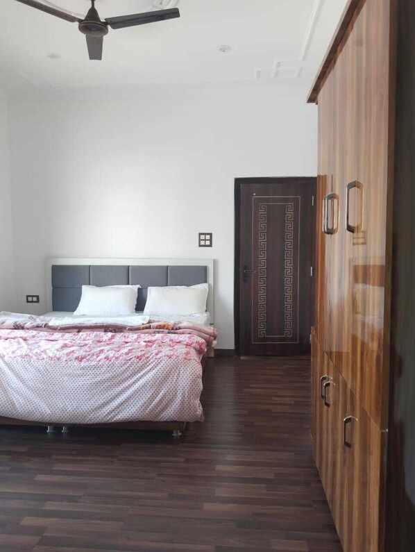 A bedroom with a bed, wooden wardrobe, and a ceiling fan.