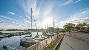 Un puerto deportivo con barcos amarrados, un paseo marítimo de madera y un ciclista en el sendero.