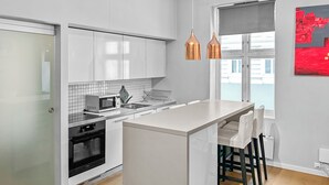 Una cocina moderna con armarios blancos, un microondas, un lavamanos y una isla grande con taburetes de bar.
