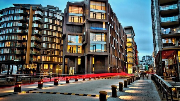 Un edificio moderno con varios pisos y balcones, que destaca por una entrada imponente con puertas de vidrio.