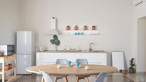 A modern kitchen with white cabinets, a white refrigerator, a microwave, and a sink. There is a dining table with chairs and a coffee maker. - Darsena Apartments by Wonderful Italy (Syracuse)