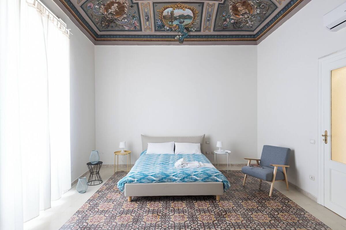 Une chambre à coucher comprenant un lit, une chaise, une table de chevet et un plafond décoratif.