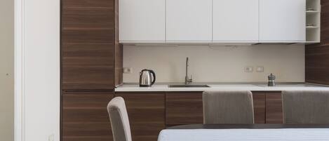 A compact kitchen with a built-in stove, a sink, and a coffee maker. There is a dining table with chairs.