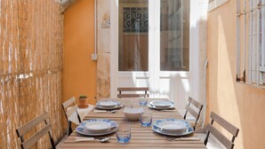 A dining table set with plates, glasses, and cutlery, surrounded by wooden chairs, in a room with an orange wall and a window with metal bars. - Darsena Apartments by Wonderful Italy (Syracuse)