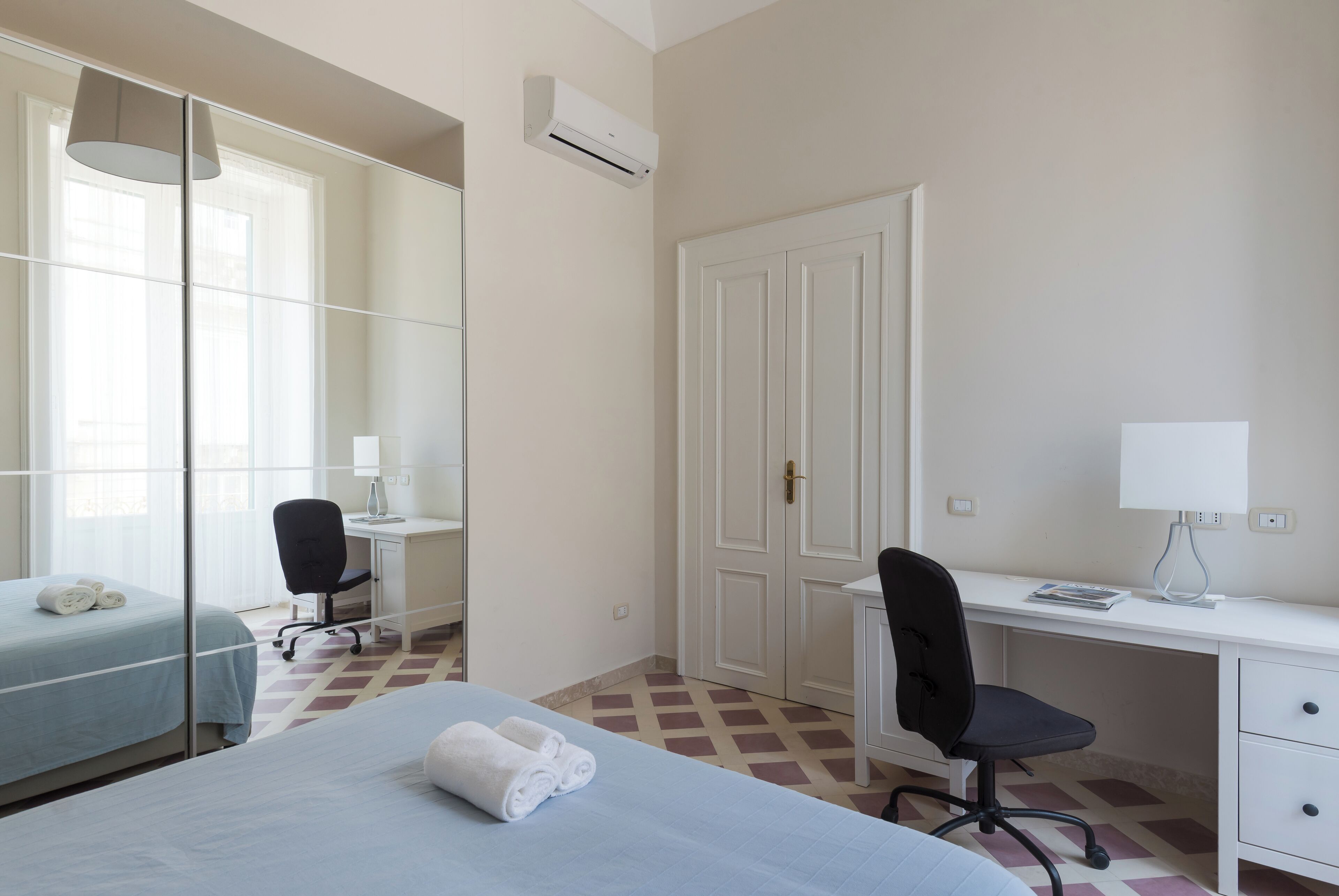 A hotel room with a bed, a desk, a chair, a wardrobe, and a mirror.