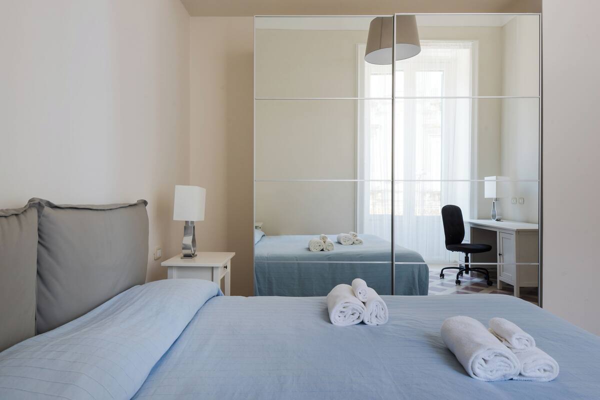 Une chambre d’hôtel avec un lit, un bureau, une chaise et un grand miroir.