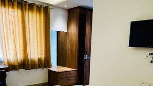 Quarto de hotel com cama, escrivaninha, cadeira, televisão e guarda-roupa.