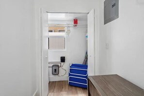 Un couloir étroit avec un plancher en bois, un meuble de rangement bleu, une porte blanche et un détecteur d’incendie au mur.