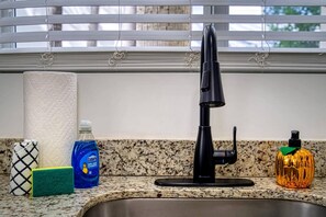A kitchen sink with a black faucet, a roll of paper towels, a blue Dawn dish soap bottle, a green sponge, and a decorative orange bottle. - Casa Roselle 3 Bedrooms Beach access (HOLLYWOOD)