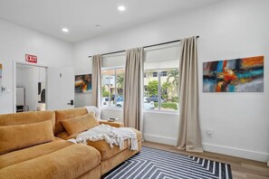 Una habitación de hotel moderna con un sofá grande, una ventana con cortinas y un cuadro en la pared.