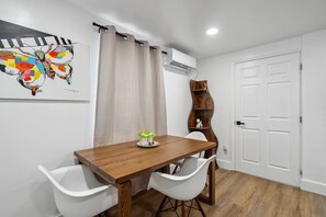 A dining area with a wooden table, white chairs, a decorative painting, a curtain, and a built-in shelf with decorative items.