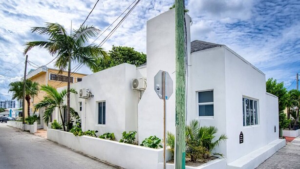 A modern white building with air conditioning units, a stop sign, and a street view with palm trees and a clear sky.