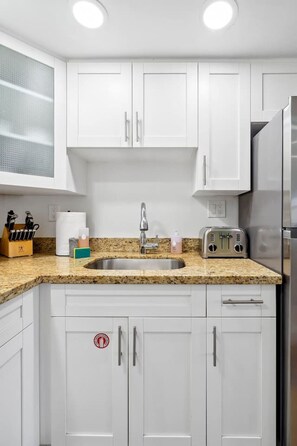 Una cocina moderna con armarios blancos, encimera de granito, pileta de acero inoxidable, tostadora y refrigerador.