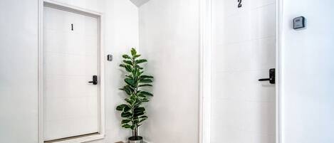 Un pasillo con dos puertas blancas, cada una con un número. Una planta en maceta se encuentra colocada entre las puertas.