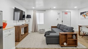A modern, well-lit living room with a grey sofa, wooden side table, and a TV mounted on the wall.