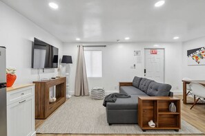 A modern, well-lit living room with a grey sofa, wooden side table, and a TV mounted on the wall. - Casa Roselle 3 Bedrooms Beach access (HOLLYWOOD)