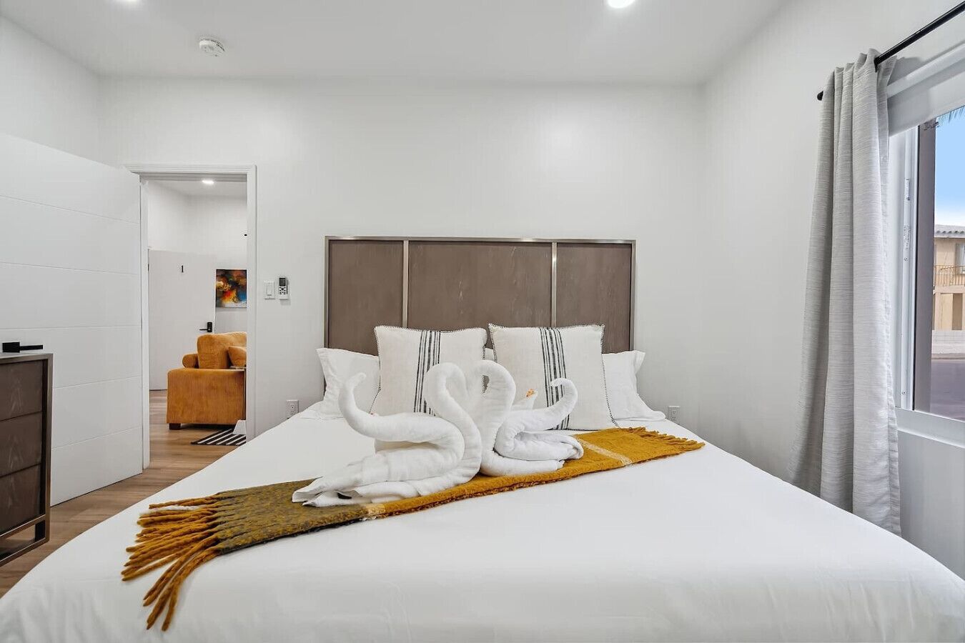 Une chambre d’hôtel moderne avec un grand lit, une tête de lit en bois et une vue sur la ville par la fenêtre.