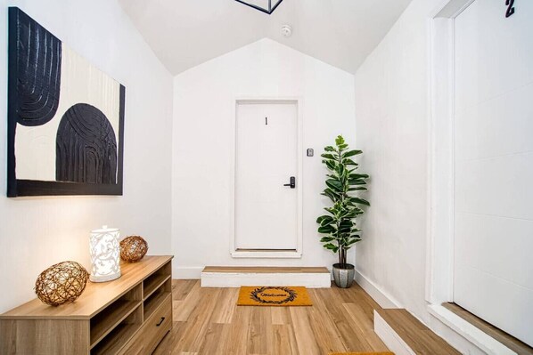 A hallway with a white door, a wooden console table with decorative items, a potted plant, and a welcome mat.
