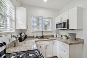 A modern kitchen with white cabinets, a granite countertop, a stove, a microwave, and a window with blinds.