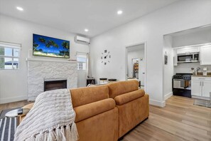 A modern living room with a fireplace, a sofa, and a kitchen area with white cabinets and a microwave. - Casa Roselle 3 Bedrooms Beach access (HOLLYWOOD)