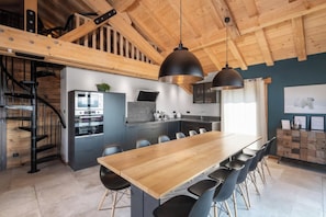 Een moderne keuken met een houten eettafel en stoelen, een inbouwoven en een trap.