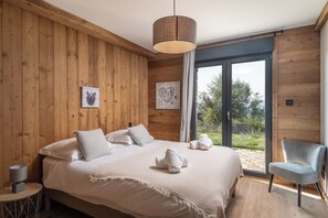 A bedroom with a large bed, wooden walls, a view through a glass door, and a chair.