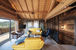 Un interior moderno con techo de madera, un sofá amarillo, una silla negra y un televisor.