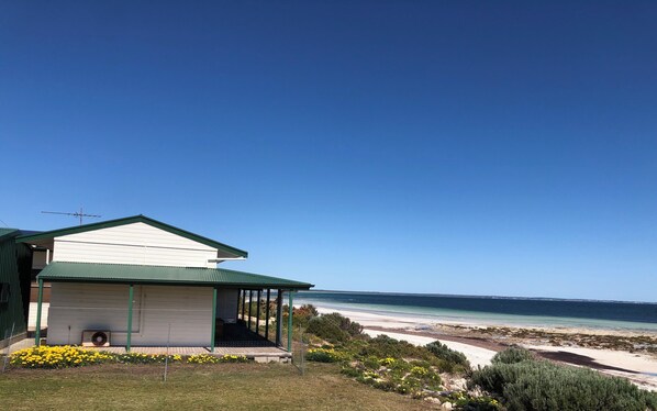 A coastal house with a green roof, a covered porch, and a view of the beach and ocean. - Cordelia and the Gull. Perfect, right on the beach, no road between you and sea. (Hardwicke Bay)