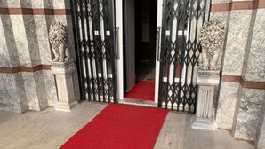 Un tapis rouge menant à une entrée fermée par un portail, de part et d’autre de laquelle se trouvent des statues de lions.