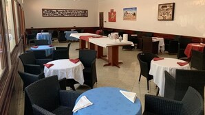 Un espace repas avec des tables et des chaises rondes, certaines agrémentées de serviettes rouges. Les murs sont ornés de tableaux encadrés et le plafond présente un motif décoratif.