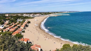 Un pueblo costero con una playa, edificios de techo rojo y un mar azul cristalino.