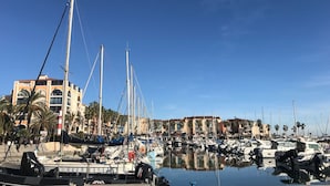 Un puerto deportivo con varias embarcaciones amarradas, un edificio con arcos y palmeras.