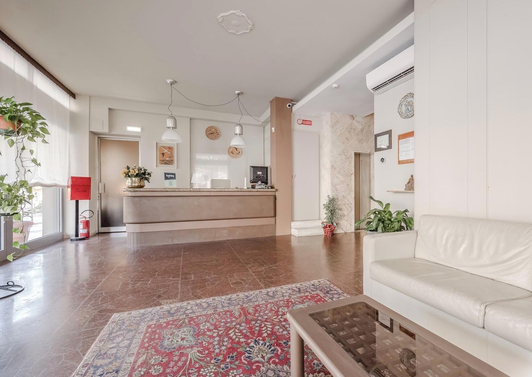A hotel lobby with a reception desk, a white sofa, a patterned rug, and a coffee table.