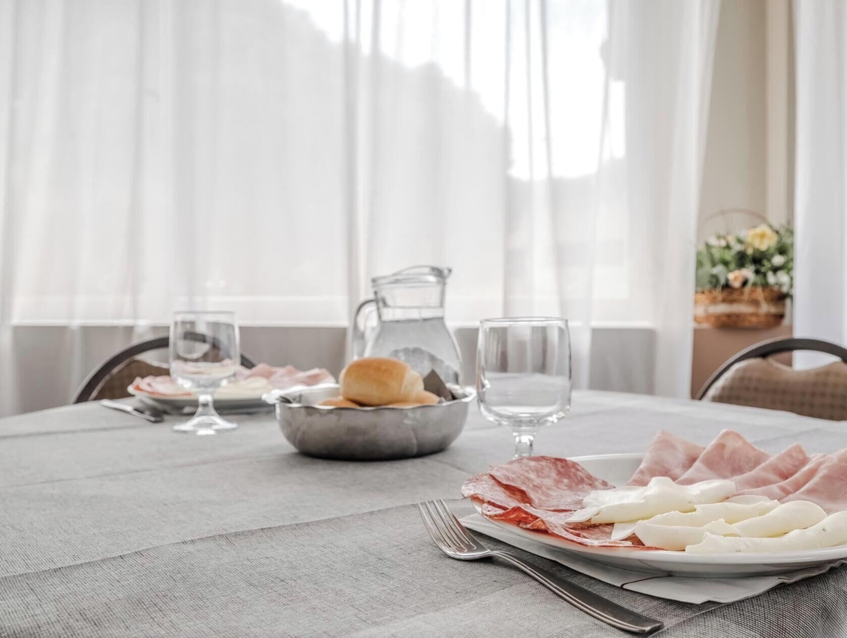 A dining table set with plates of cured meats, a pitcher, and glasses.