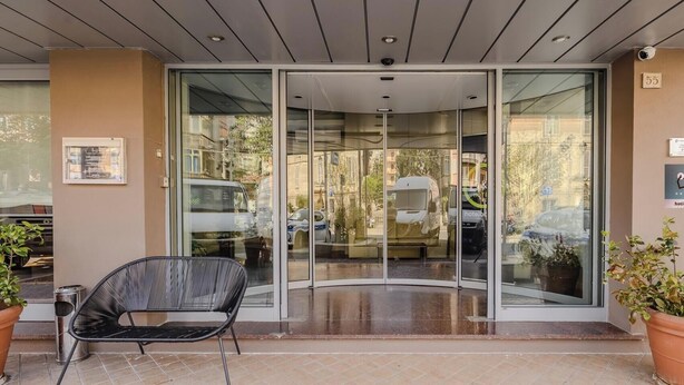 A hotel entrance with a glass door, a black chair, and a potted plant. - Hotiday Celle Ligure (Celle Ligure)