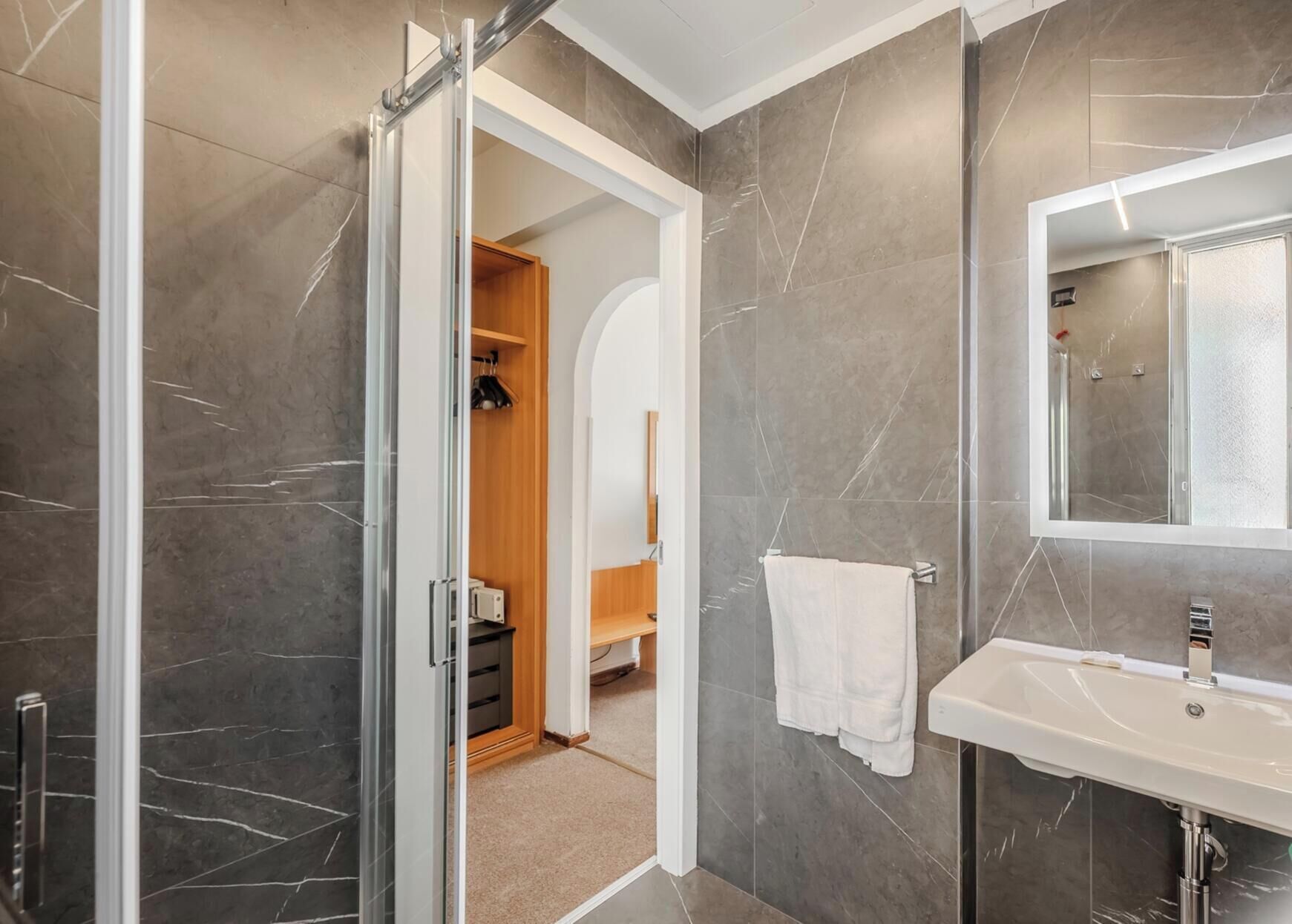 Un bagno moderno con box doccia in vetro, un lavandino bianco e uno specchio.