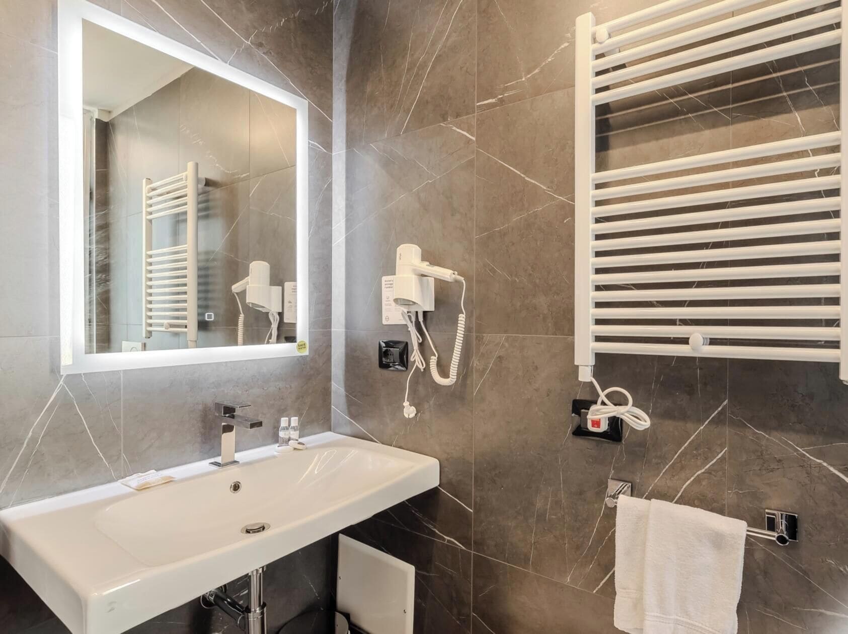 Un baño con lavamanos blanco, un espejo, un perchero y una toalla colgada.