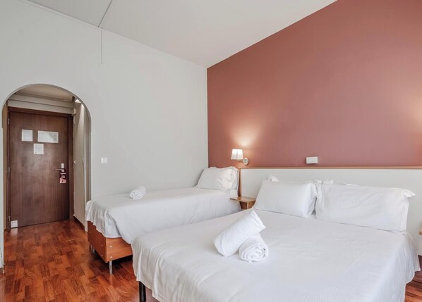 A hotel room with two beds, a wooden floor, a door with a sign, and a wall-mounted lamp. - Hotiday Celle Ligure (Celle Ligure)