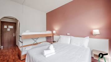 Habitación de hotel con literas, una cama individual, suelo de madera, una puerta con un aviso y dos lámparas fijadas a la pared.