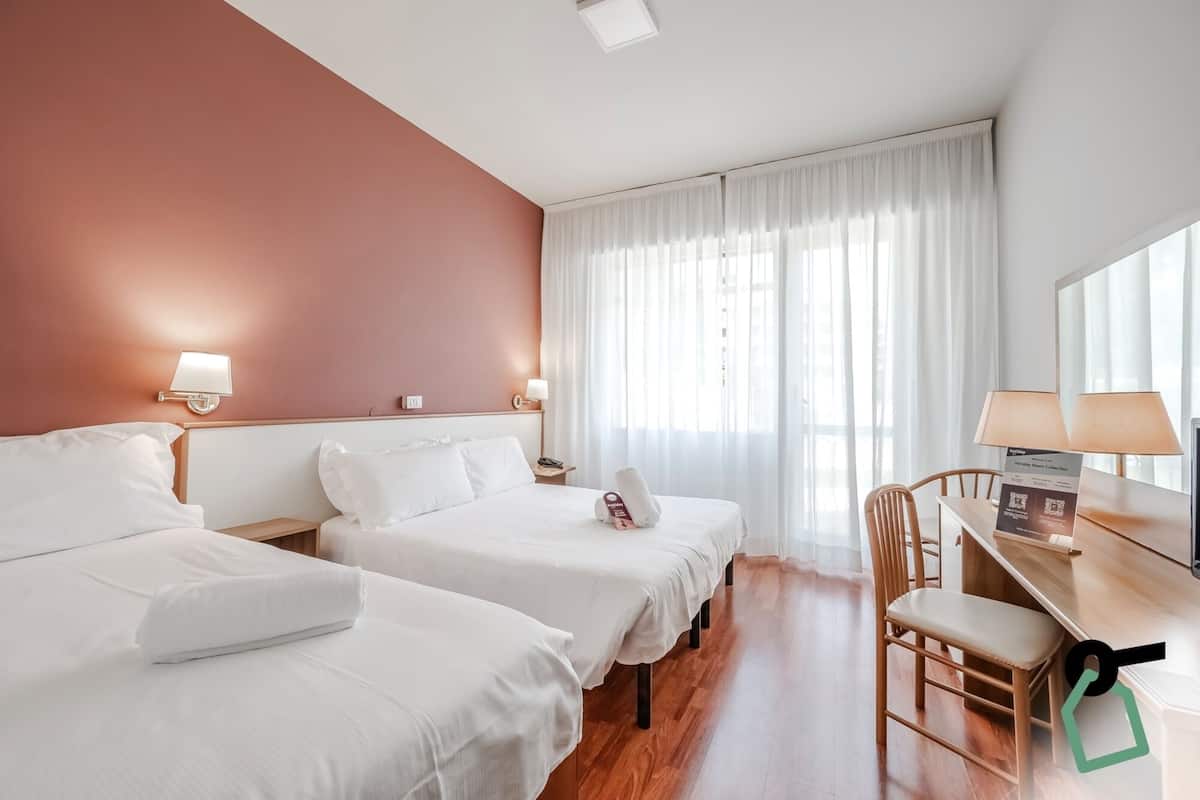 A hotel room with two beds, a desk, and a chair.