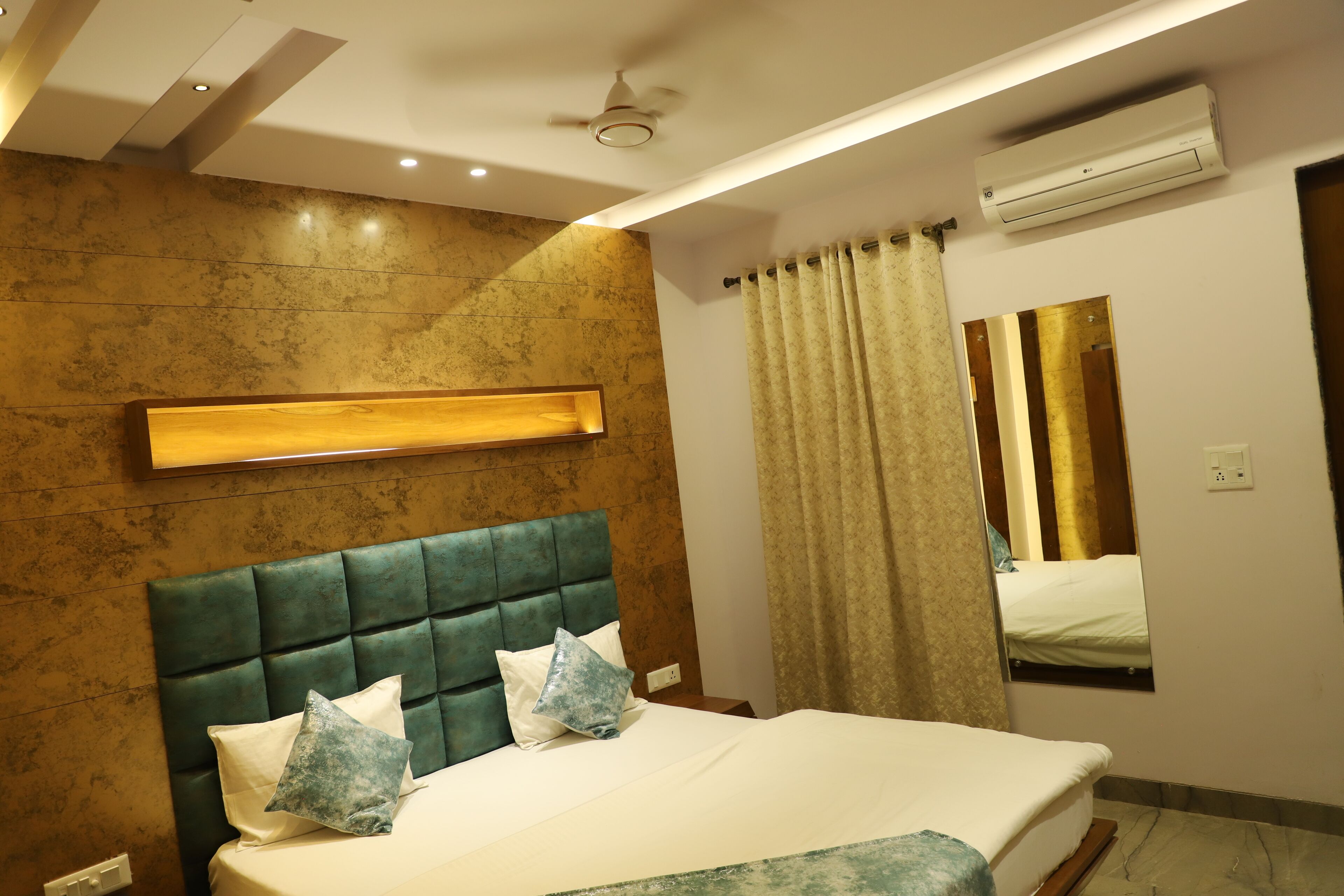 A modern hotel room with a large bed, a headboard, a mirror, and an air conditioning unit.